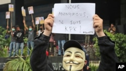 FILE - A masked supporter of Indonesian Corruption Eradication Commission (KPK) holds up a poster that reads "I am KPK" during a protest against the arrest of the deputy head of the Corruption Eradication Commission Bambang Widjojanto by the police, outside the commission's office in Jakarta, Jan. 23, 2015. 