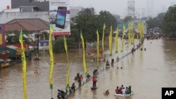 Warga mengarungi daerah yang banjir di Jakarta (13/1). (AP/Achmad Ibrahim)