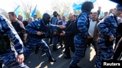 FILE - Members of the Russian Interior Ministry security forces attempt to block the way for Crimean Tatars to cross a checkpoint connecting Crimea and Ukraine's Kherson region to meet with Tatar leader Mustafa Dzhemilev, near Armyansk May 3, 2014.