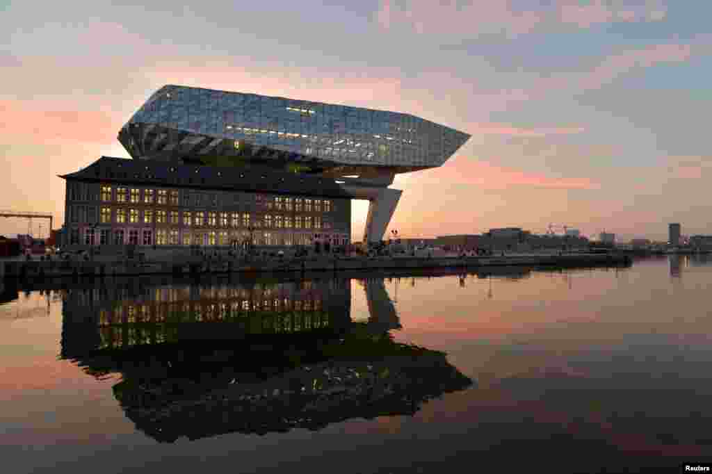 The sun rises behind the new headquarters for the Antwerp Port Authority on the Kattendijk dock, the Port House, a monumental design by Zaha Hadid Architects in Antwerp, Belgium.