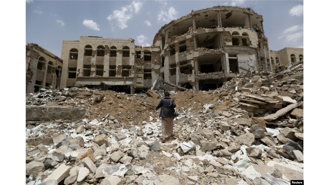 FILE - An Iranian-allied Houthi militant walks in front of a government compound, destroyed by recent Saudi-led airstrikes, in Yemen's northwestern city of Amran, July 27, 2015.