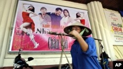 A Vietnamese vendor passes a movie theater advertising the latest Vietnamese blockbuster film