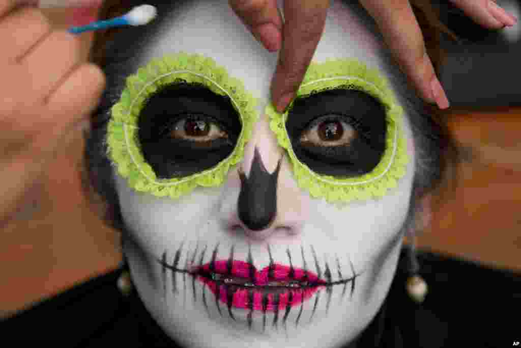 A woman has her makeup applied as she waits for the start of a Day of the Dead parade to begin along Mexico City's main Reforma Avenue, Oct. 28, 2017.