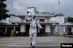 Seorang petugas mengenakan alat pelindung diri (APD) menyemprotkan disinfektan di depan Kantor Walikota yang ditutup akibat pandemi COVID-19 yang terus berlanjut di Bandung, provinsi Jawa Barat, 28 Juni 2021. (REUTERS)