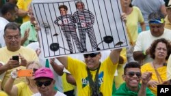 A demonstrator holds a poster with the photo of Brazilian president Dilma Rousseff and former President Luiz Inacio Lula da Silva in prison stripes during a protest on Copacabana beach in Rio de Janeiro, Brazil, March 13, 2016.