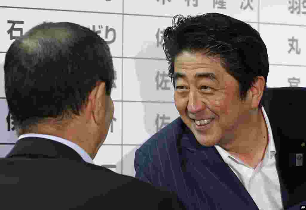 Japanese Prime Minister Shinzo Abe exchanges smiles with Secretary General Shigeru Ishiba of the ruling Liberal Democratic Party during ballot counting at the party headquarters in Tokyo, July 21, 2013. 