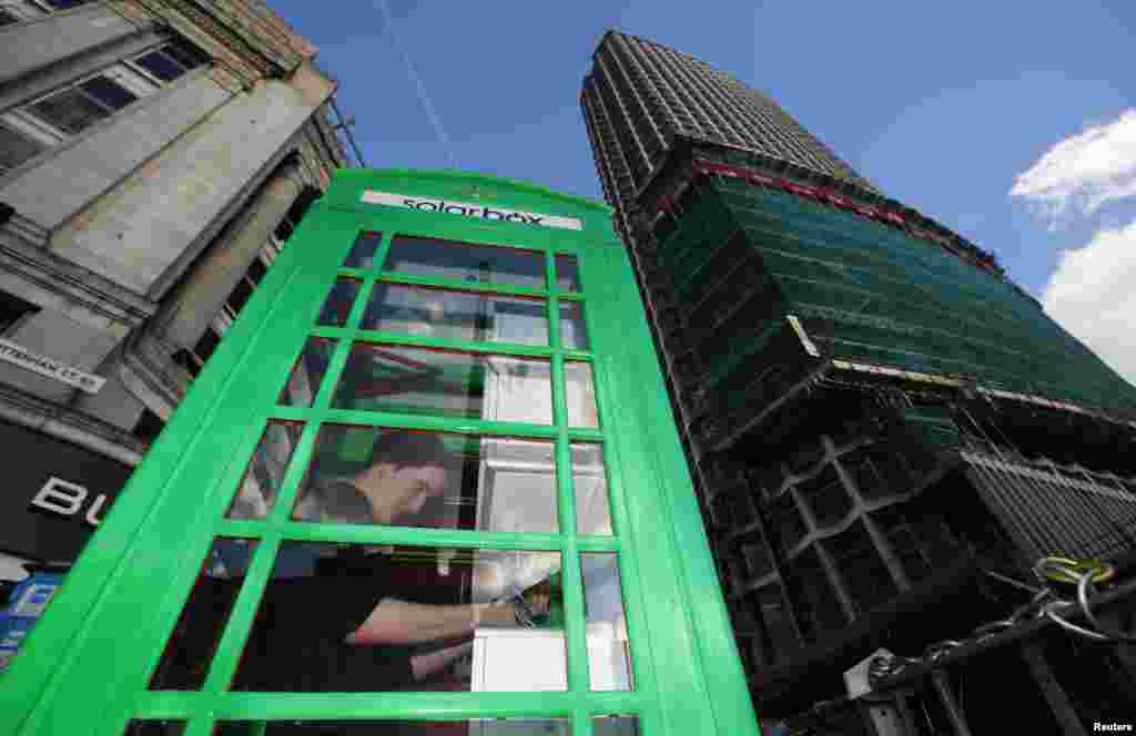 A man uses a green &quot;Solarbox&quot; to charge his phone in central London. Some of London&#39;s famous red telephone boxes are going green, changing into free, sun-powered mobile chargers to provide a carbon-neutral source of energy in the city. 