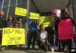 Protesters hold up signs outside a courthouse, April 14, 2017, where U.S. District Court Judge William Orrick ruled on a lawsuit challenging President Donald Trump's executive order to withhold funding from sanctuary cities.