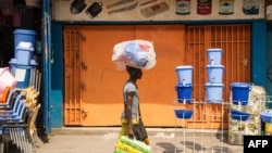 Un homme porte sur le tète un sac plastique rempli des marchandises, devant une boutique fermée au marché central de Kinshasa, RDC, 7 aout 2016.