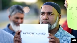 FILE - A man holds a sign supporting Ahmed Mohamed, who was arrested when teachers and police mistook a clock he built and brought to school for a bomb.