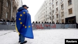 یک تظاهرکننده اوکراینی در موافقت با پیوستن کشورش به اتحادیه اروپا، با پرچم اتحادیه در برابر ساختمان وزارت کشور در کیف - ۱۲ دسامبر 