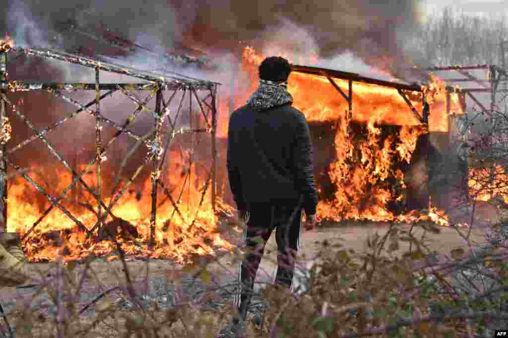 Seorang migran memperhatikan gubuk yang terbakar saat pembongkaran separuh kamp migran &quot;Jungle&quot; di kota pelabuhan Perancis utara, Calais. Bentrokan pecah antara polisi anti huru-hara dan migran sementara bulldozer bergerak ke kawasan kumuh di tepi Calais yang dikenal sebagai &quot;Jungle&quot; dan mulai menghancurkan ratusan tempat penampungan sementara.