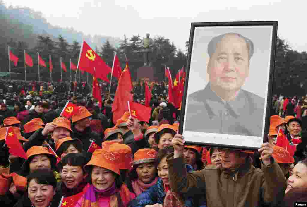 Um homem enverga um retrato de Mao Zedong enquanto ele e outros se reúnem em frente à estátua gigante de de Mao para celebrar o seu 120&ordm; aniversário na sua cidade natal, Shaoshan, Dez. 26, 2013.