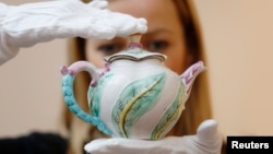 FILE - A Sotheby's employee poses with a Chelsea scolopendrium-molded teapot (dated c.1750), believed to be the only surviving example of this pattern, at Sotheby's auction house in London, May 9, 2014.