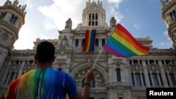 A man waves a flag as a giant rainbow flag hangs over the facade of city hall in Madrid, Spain, June 26, 2017.