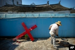 FILE - A church member shovels cement mix preparing to re-mount a cross on a Protestant church, which had been forcibly pulled down by Chinese government workers in Taitou Village, eastern China, July 29, 2015.