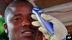 Nhân viên y tế đo nhiệt độ của một người đàn ông trước khi cho phép vào trung tâm thương mại trong lúc nỗi sợ hãi về sự lây lan của virus Ebola gia tăng ở thành phố Monrovia, Liberia.