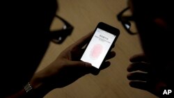 FILE - An Apple employee, right, instructs a journalist on the use of the fingerprint scanner technology built into the company's iPhone during a media event in Beijing, Sept. 11, 2013. Watchdog groups are concerned that U.S. Customs and Border Protection agents are searching the phones and other digital devices of international travelers at border checkpoints in U.S. airports. 