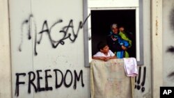 在希腊伊多梅尼岛的一个庇护所里一名妇女怀抱儿童站在窗前。（2016年5月3日）