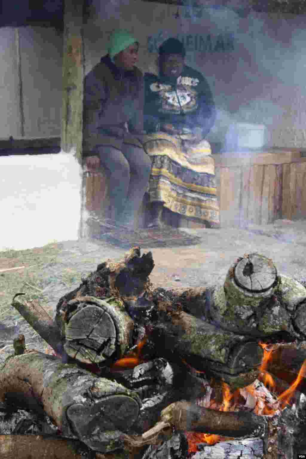 Lungiswa warms at a fire at the home, with a fellow resident. (VOA/ D. Taylor) 