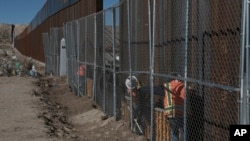 FILE - Workers continue work raising a taller fence on the Mexico-U.S. border separating the towns of Anapra, Mexico, and Sunland Park, New Mexico, Jan. 25, 2017. 