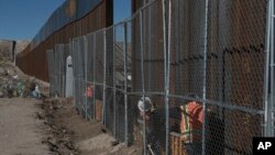 Para pekerja melanjutkan pembangunan pagar yang lebih tinggi di perbatasan Meksiko-AS yang memisahkan kota Anapra, Meksiko dan Sunland Park, New Mexico, AS (25/1). (AP/Christian Torres) 