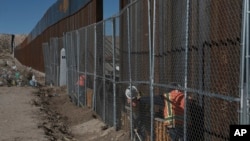 FILE - Workers continue work raising a taller fence in the Mexico-U.S. border separating the towns of Anapra, Mexico, and Sunland Park, New Mexico, Jan. 25, 2017. 