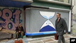 A shoeshine man sits in front of a closed shop with graffiti sprayed on its shutters in central Athens, Greece, March 12, 2012.