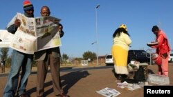 Men read a newspaper next to a stall in Soweto, South Africa, June 24, 2013.