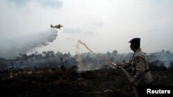 지난달 말 인도네시아 수마트라 인근에서 불타는 이탄지에 소화액을 분무하고 있는 경찰관 위로 소방항공기가 물을 쏟아내리고 있다.