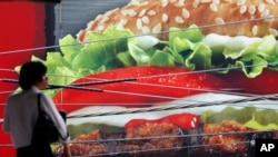 Advertisers make hamburgers look SO good! Here, a man stands in front of an advertisement of a hamburger shop in Tokyo, June 2014. (AP Photo/Shizuo Kambayashi)