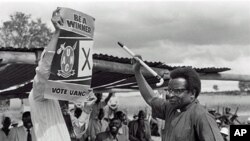 Bishop Abel Muzorewa, member of executive council and leader of UANC, shows voters how to vote by signing a cross near crest of his party during Rhodesian general elections, 19 Apr 1979