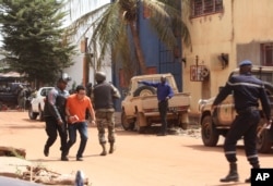 A soldier, left, assists a hostage, second left, to leave the scene, from the Radisson Blu hotel to safety after gunmen attacked the hotel in Bamako, Mali, Nov. 20, 2015.
