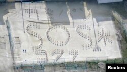 Những chữ "Giấy (vệ sinh), Bánh mỳ, Nước và SOS" được xếp bằng ghế ở sân chơi của trường trung học Kumamoto Kokufu sau trận động đất ở Kumamoto, miền nam Nhật Bản. Ảnh được chụp bởi hãng thông tấn Kyodo ngày 17 tháng 4 năm 2016.