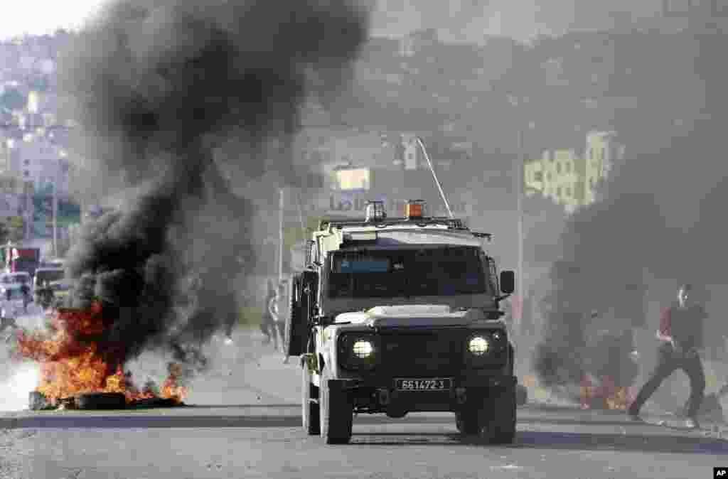 Sebuah kendaraan tentara Israel melewati ban-ban yang terbakar dalam sebuah operasi pencarian di kamp pengungsi di Tepi Barat kota Jenin, 17 Juni 2014.