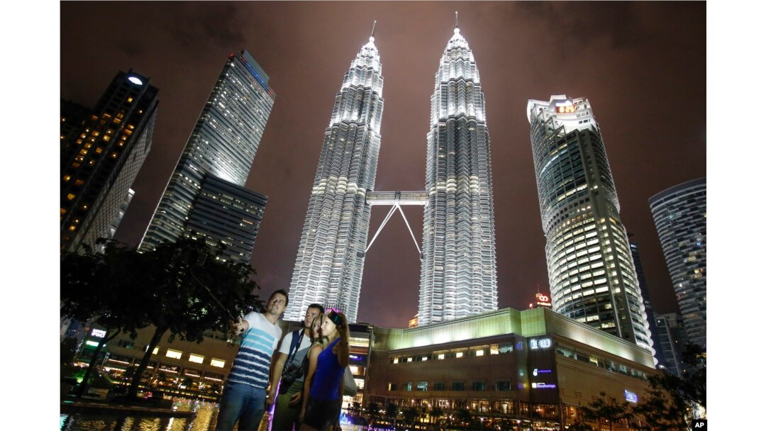 Turis mengambil foto kenang-kenangan di depan gedung ikonik Malaysia, Menara Kembar Petronas di Kuala Lumpur, Malaysia, Kamis, 14 Januari 2016. (Foto: AP)