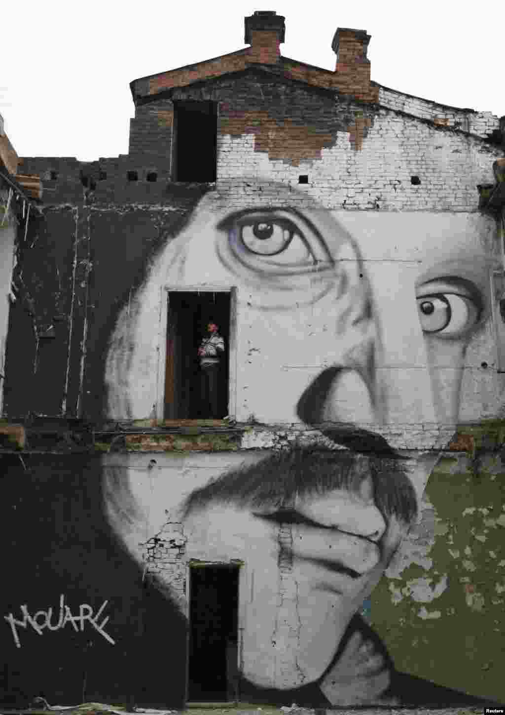 A visitor stands in a doorway of an abandoned house painted with a portrait of Russian actor Alexander Kaidanovsky by French artist The Mouarf, in the centre of Russia's Siberian city of Krasnoyarsk