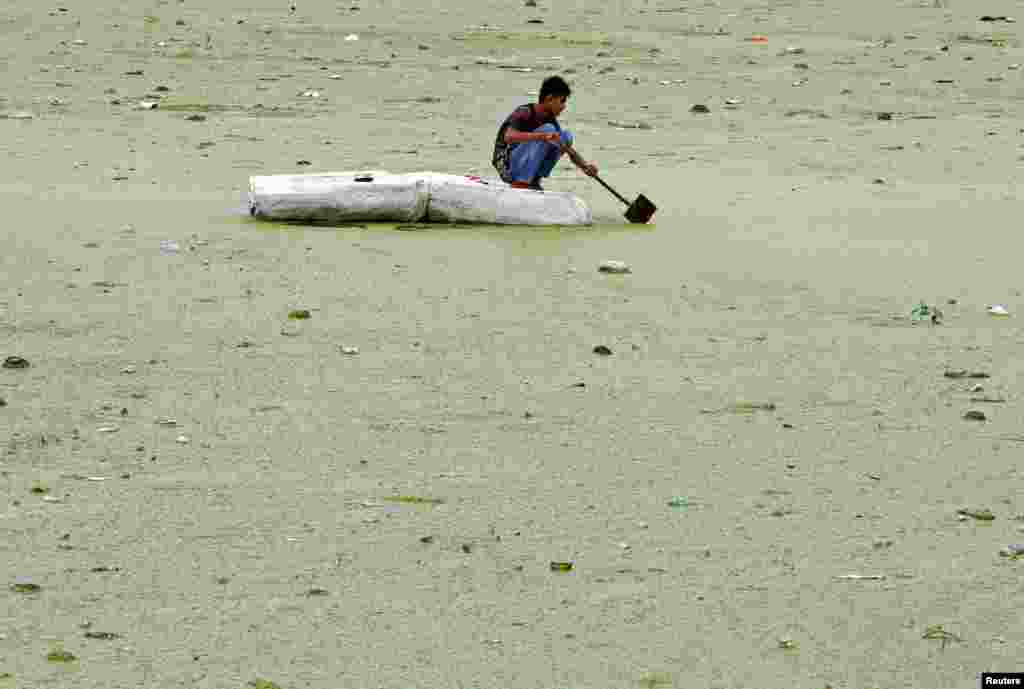 인도 아마다바드의 사바르마티 강이 녹조로 뒤덮힌 가운데, 한 소년이 급조한 뗏목을 타고 있다.
