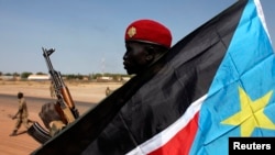 A soldier with the Sudan People's Liberation Army - the army of the Republic of South Sudan - is pictured behind a South Sudan flag as he sits on the back of a pick-up truck in Bentiu, Unity state, Jan. 12, 2014.