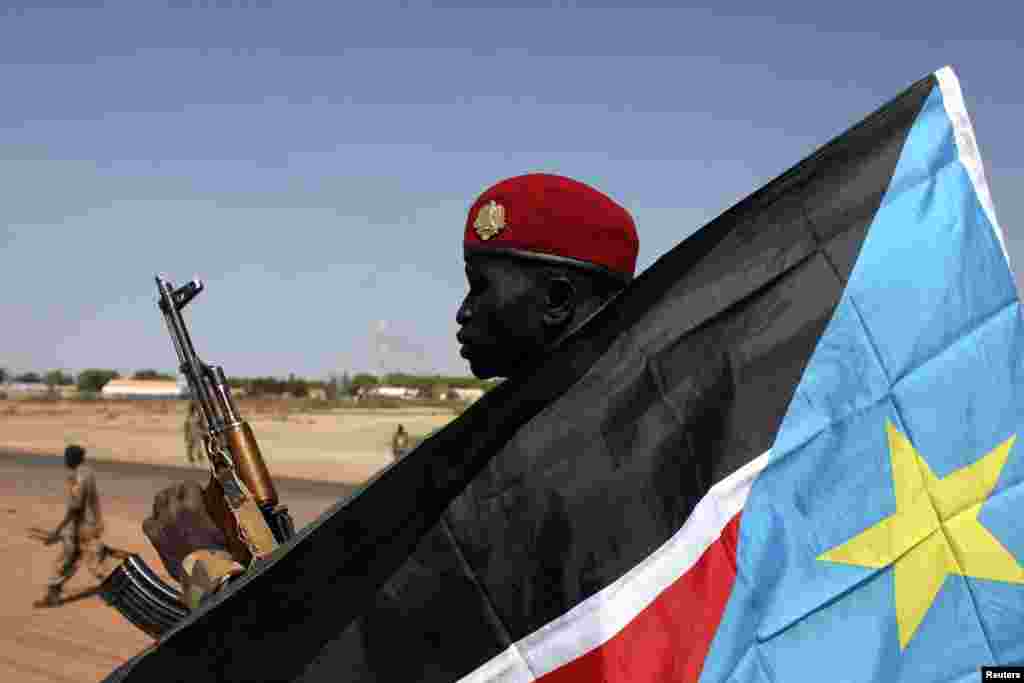 A soldier with the Sudan People&#39;s Liberation Army - the army of the Republic of South Sudan - is pictured behind a South Sudan flag as he sits on the back of a pick-up truck in Bentiu, Unity state, Jan. 12, 2014.Bentiu was recaptured by government forces on Jan. 10.