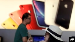 A customer looks at her iPhone in a store of U.S. tech company Apple in Beijing, May 10, 2019. China says it is imposing tariffs on $60 billion worth of imports from the United States.