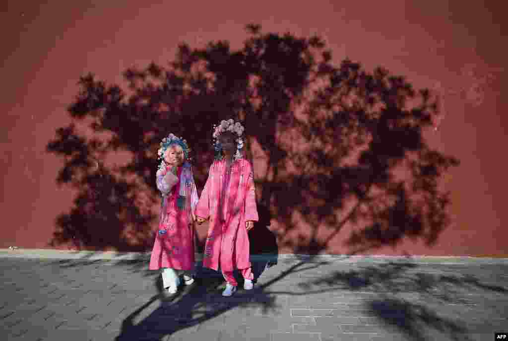 Two people wearing special clothing poses for a photographer under the shade of a tree in Beijing, China.