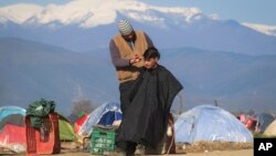 A man gets a haircut from a fellow migrant at the northern Greek border point of Idomeni, Greece, Sunday, March 20, 2016. 