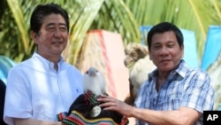 Philippine President Rodrigo Duterte, right, hands over a Philippine Eagle stuffed toy named Sakura to Japan's Prime Minister Shinzo Abe during the ceremonial eagle naming at the garden area of Waterfront Insular Hotel in Davao City, southern Philippines,