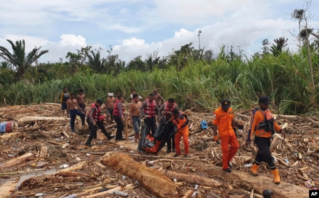 In this photo provided by National Search and Rescue Agency, the agency's personnel and police carry the body of flood victim at Sentani, Papua Province, Indonesia, March 17, 2019.