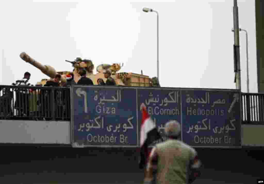 An anti-government protester looks towards an Egyptian tank on a bridge near Tahrir, or Liberation square in Cairo, Egypt, Thursday, Feb. 3, 2011. Another bout of heavy gunfire and clashes erupted Thursday around dusk in the Cairo square at the center of 
