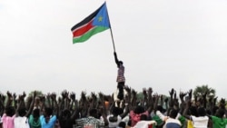 A man holds up South Sudan's new flag as South Sudanese children rehearse their dance routine, to be performed at half time during South Sudan's national soccer team's match with Kenya as part of the independence day celebrations. Photo by Paul Banks, 