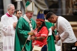 Masyarakat adat, beberapa dengan wajah dicat dan mengenakan hiasan kepala, berdiri di sebelah Paus Fransiskus saat misa untuk Amazon di Basilika Santo Petrus, di Vatikan, 6 Oktober 2019. (Foto: AP)