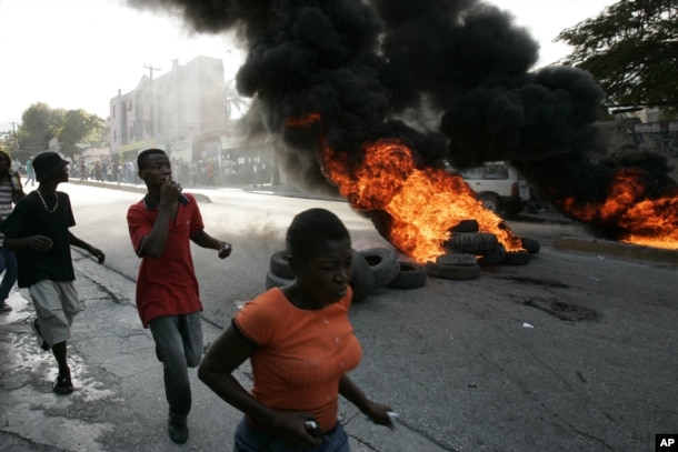FILE - Local residents run past burning tires outside the Delmas police station in Port-au-Prince, Dec 20, 2006. Riots erupted after residents surrounded the police station throwing stones and bottles demanding that the police hand over two suspected kidnappers to lynch them.