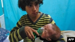 叙利亚首都大马士革郊区东古塔杜马镇遭到毒气袭击，一名男孩在一家临时医院抱着戴上氧气面罩的婴孩(2018年1月22日资料照片)